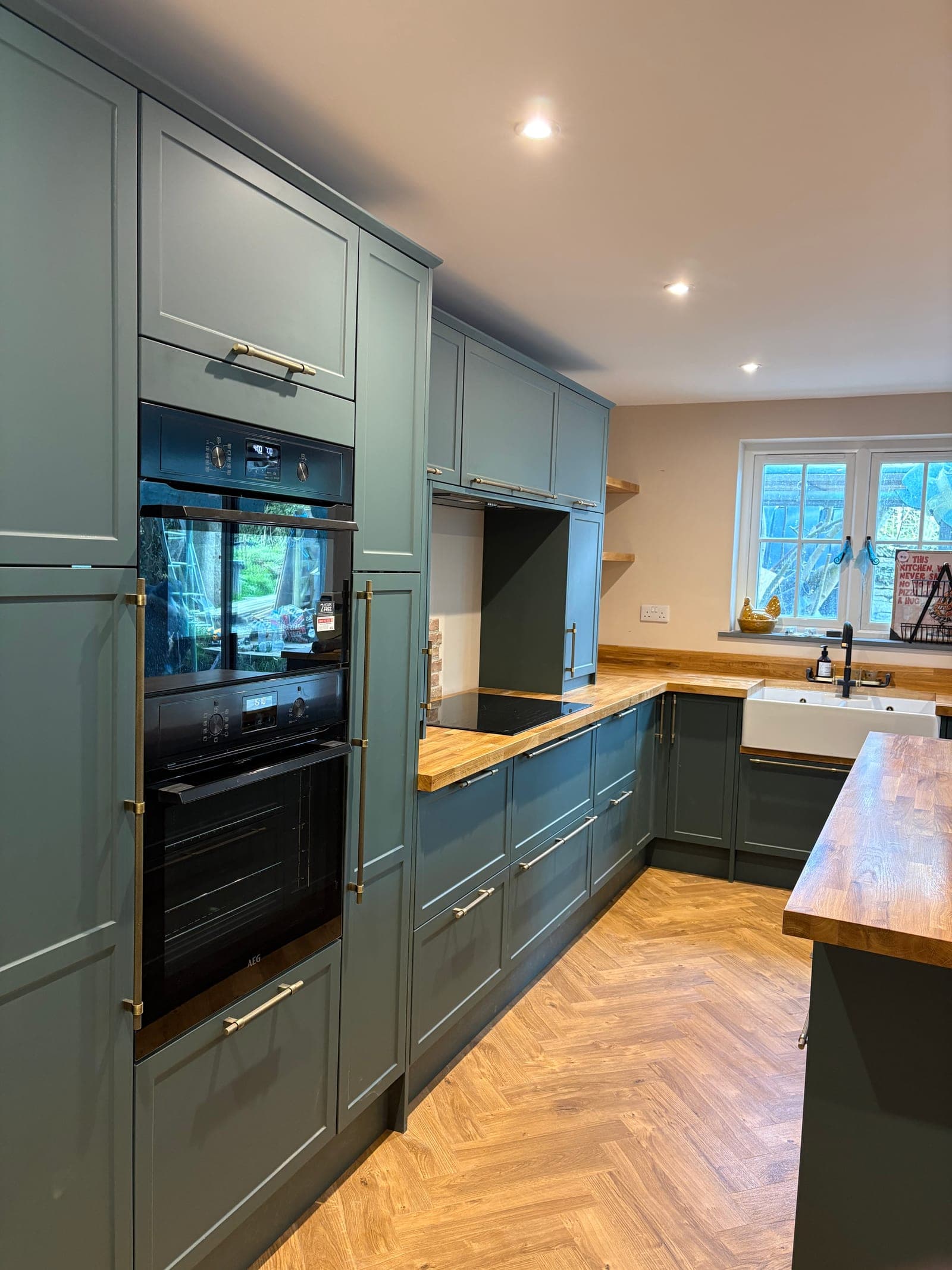 Renovated kitchen in a Cornish home with green shaker units, oak worktops and herringbone flooring